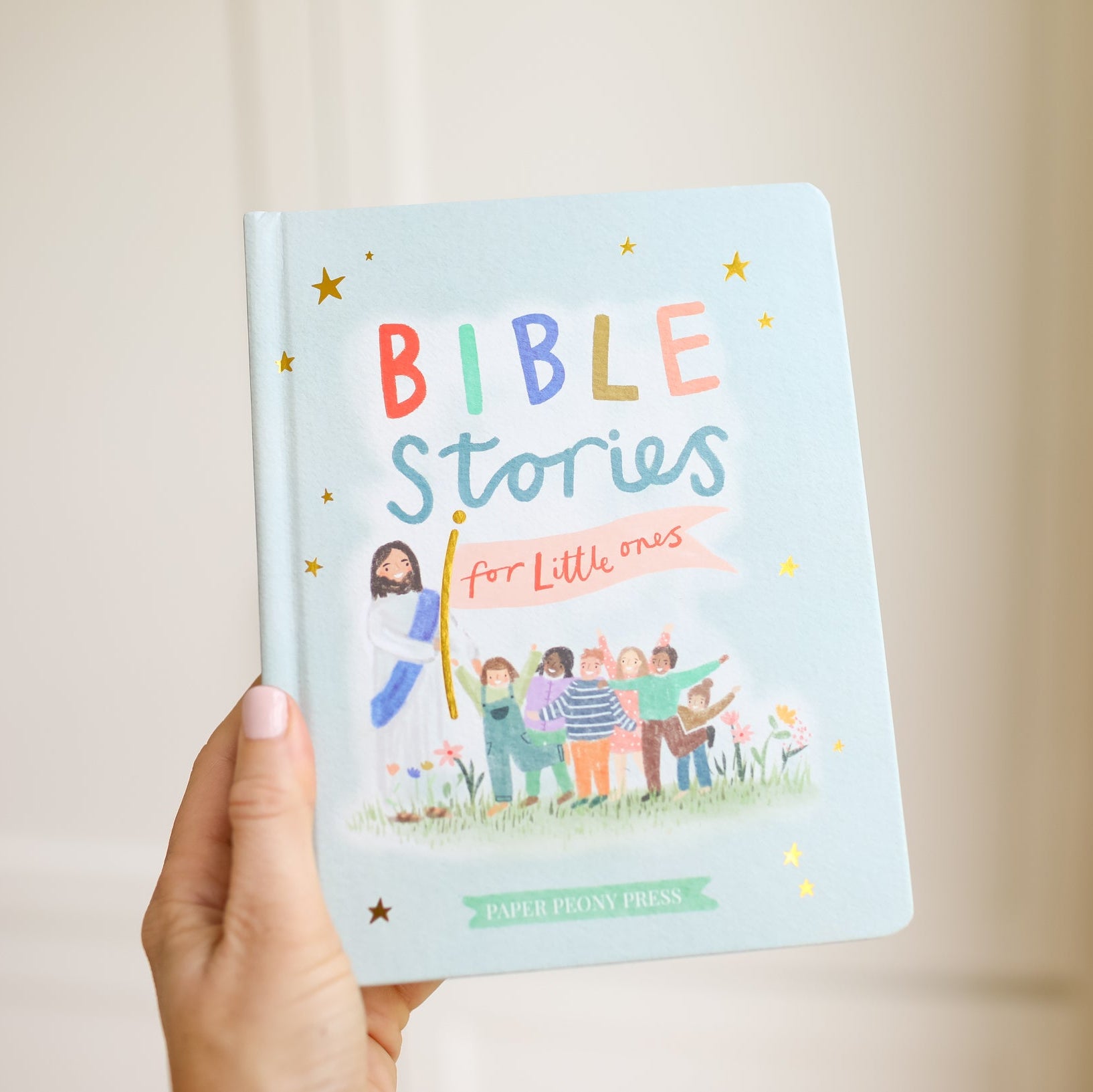 Book titled 'Bible Stories for Little Ones' held by a hand against a neutral background
