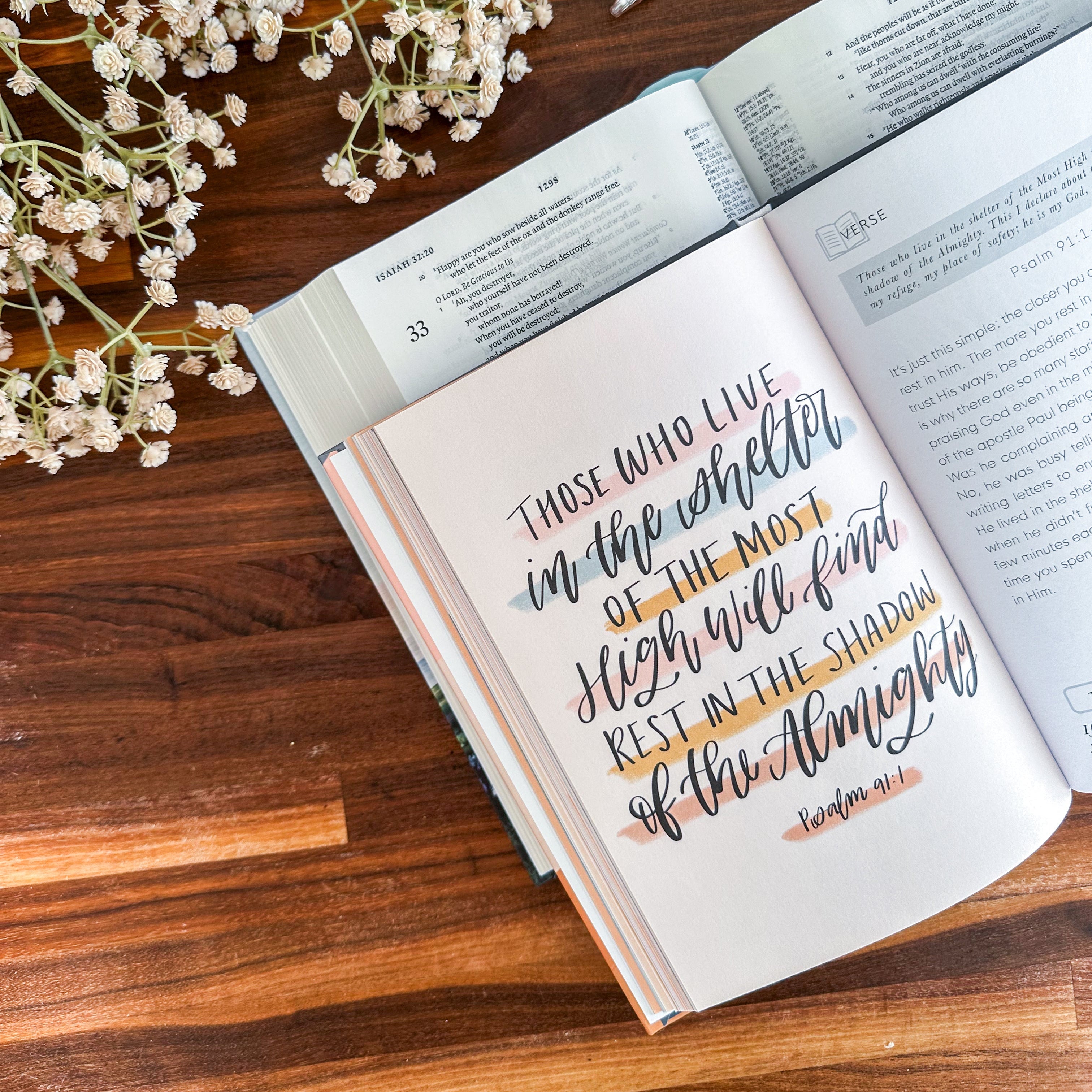 Open book with inspirational quote on a wooden surface with flowers and pens.