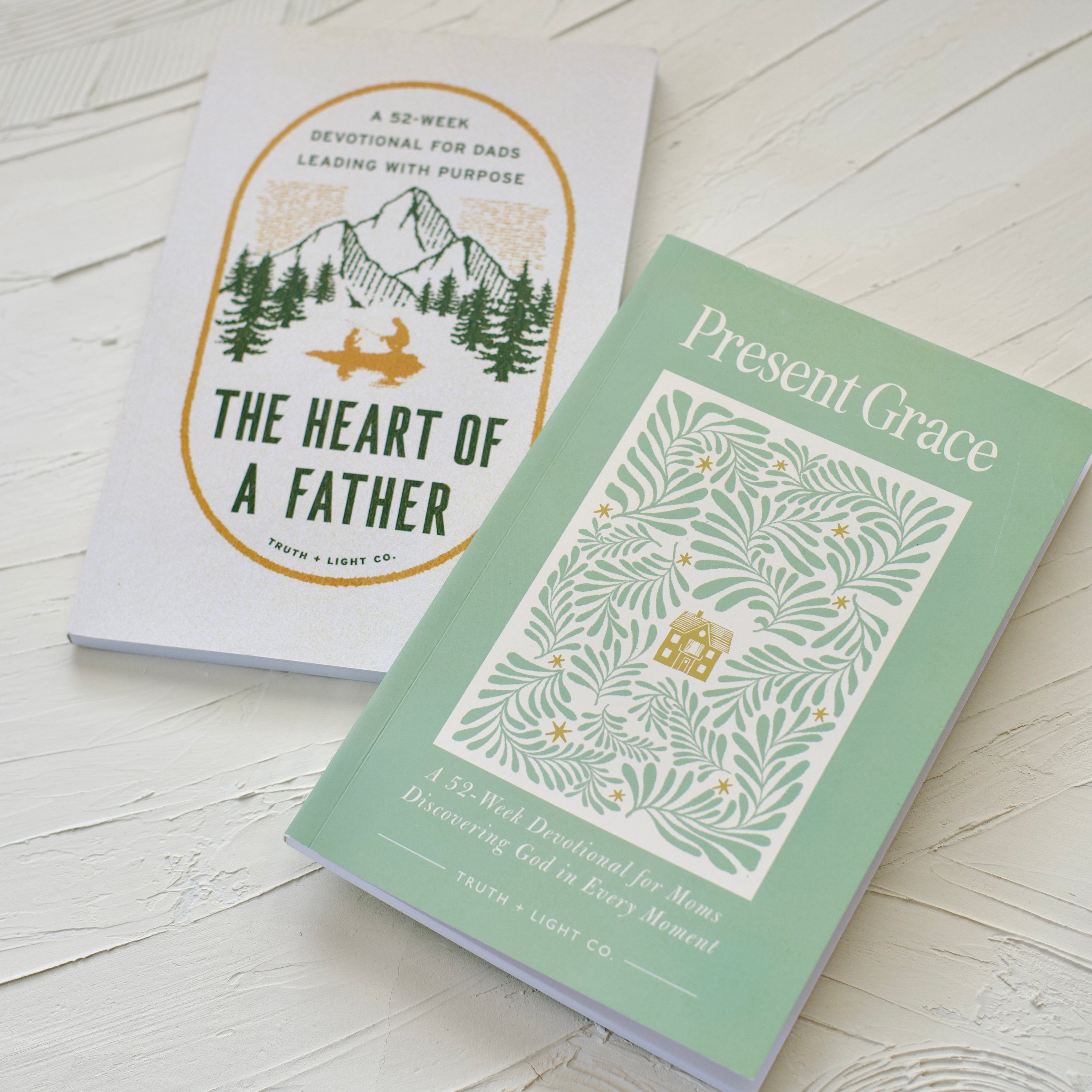 Two books titled 'The Heart of a Father' and 'Present Grace' on a light wooden surface.