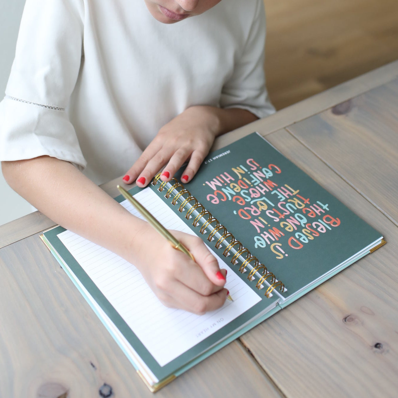 Young girl writing in a notebook with a pink headband in a home setting