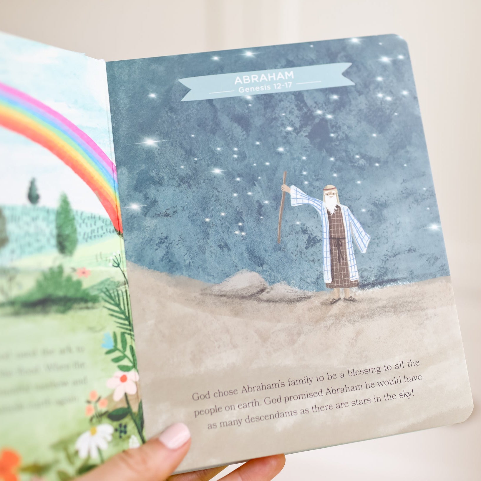 Illustrated book with a rainbow and a character standing on a mountain, held by a hand.
