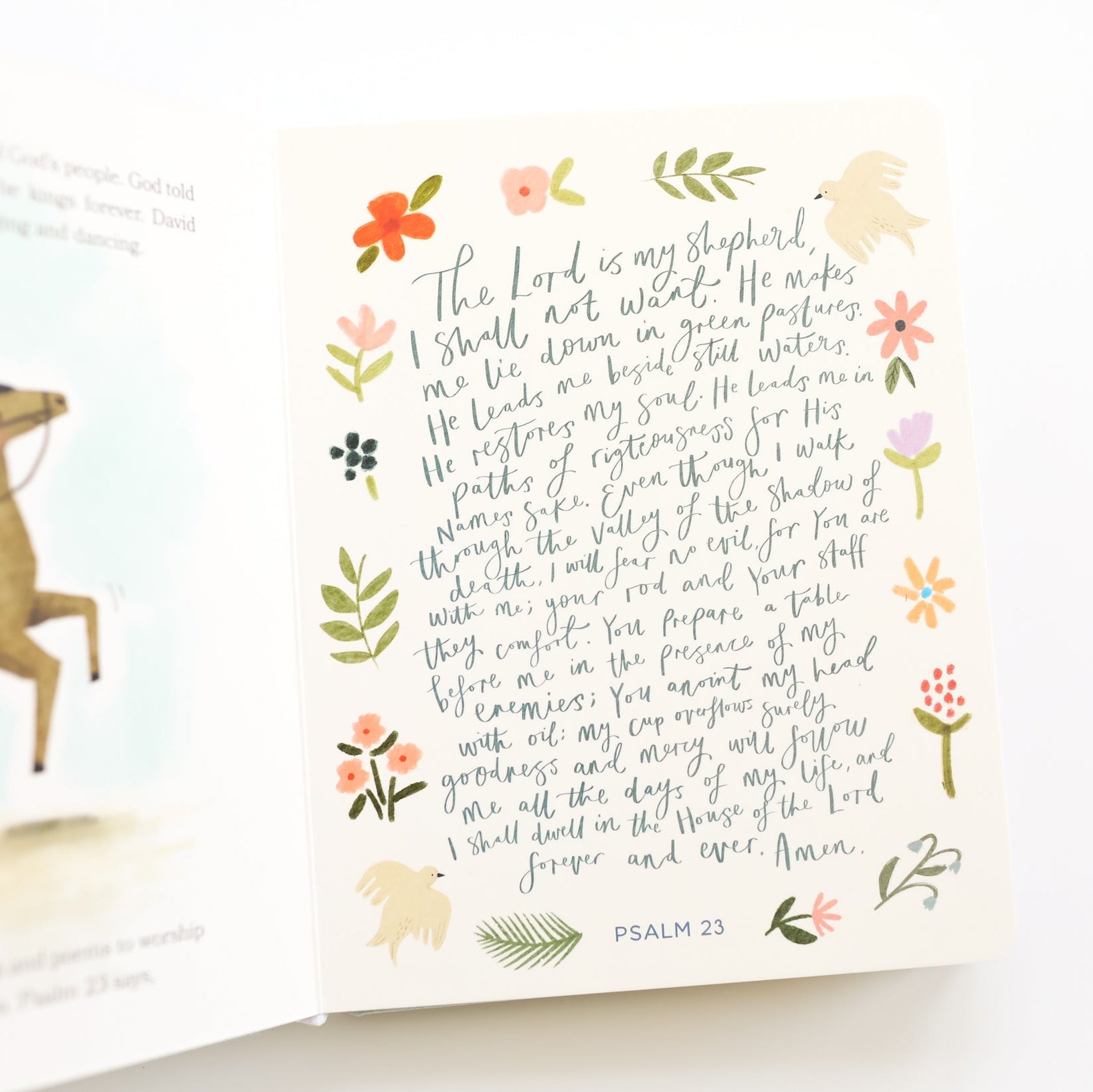 A cream-colored Bible verse card featuring Psalm 22 in elegant cursive script, surrounded by delicate hand-drawn floral and botanical illustrations. The card is shown standing upright in front of an open book page with a horse illustration.