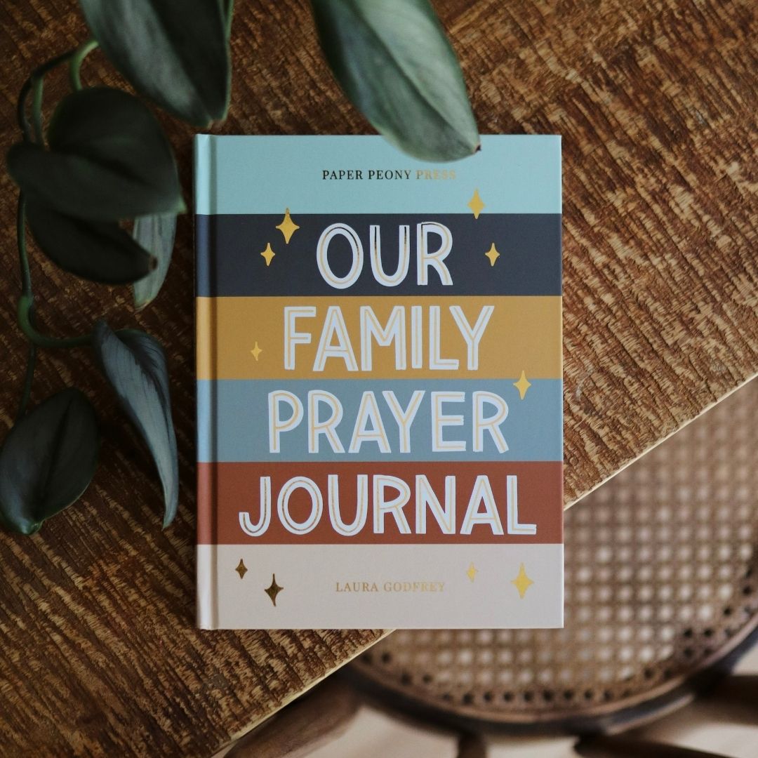 Book titled 'Our Family Prayer Journal' on a wooden surface with plants.