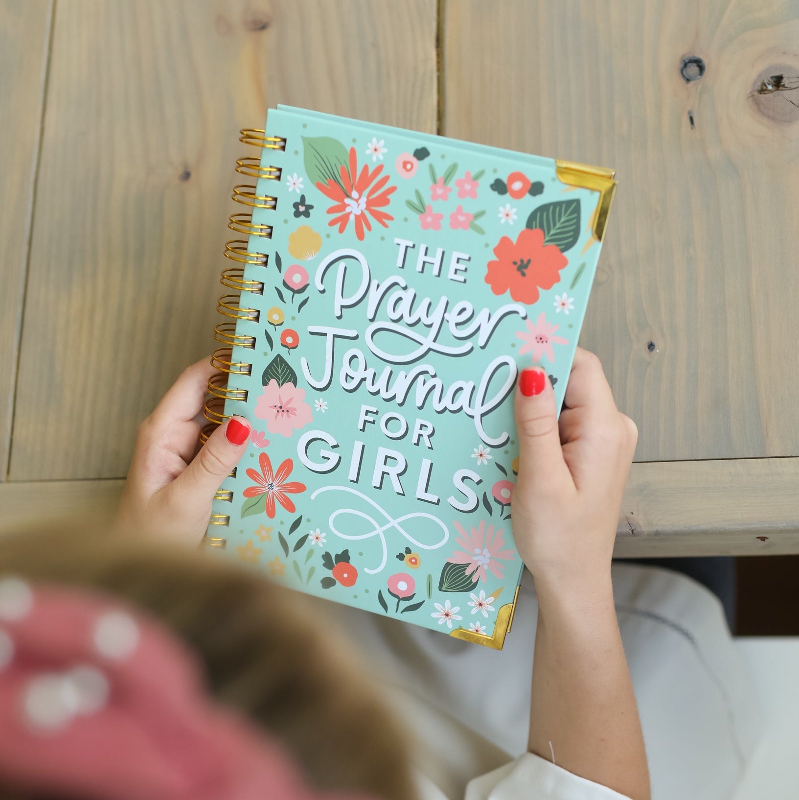 Person holding a 'The Prayer Journal for Girls' book with floral design on a wooden surface