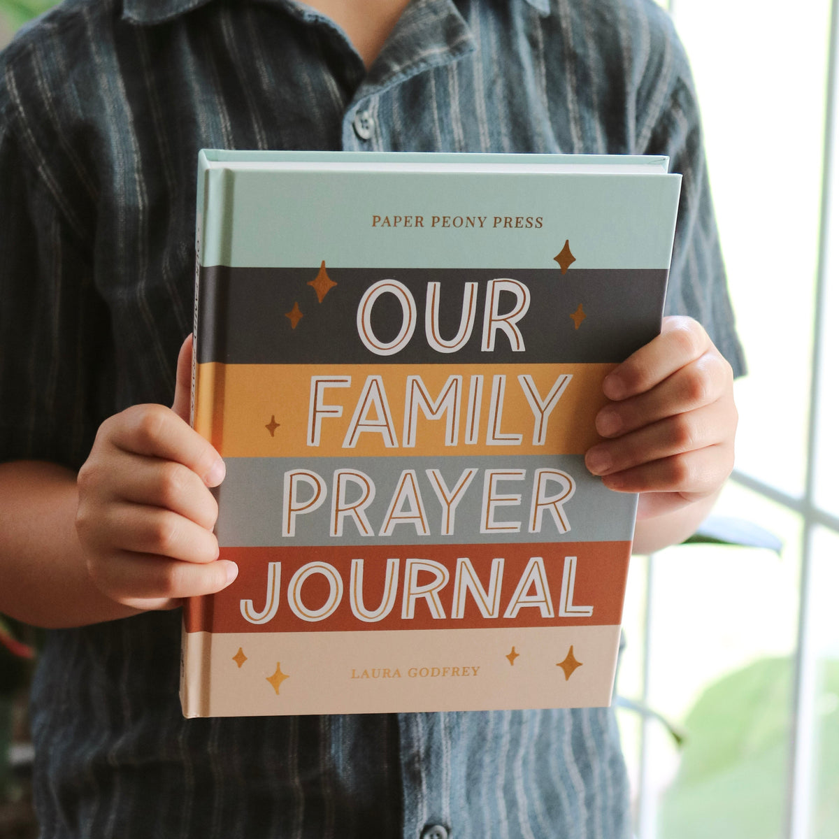 Child holding a 'Our Family Prayer Journal' book with a blurred background