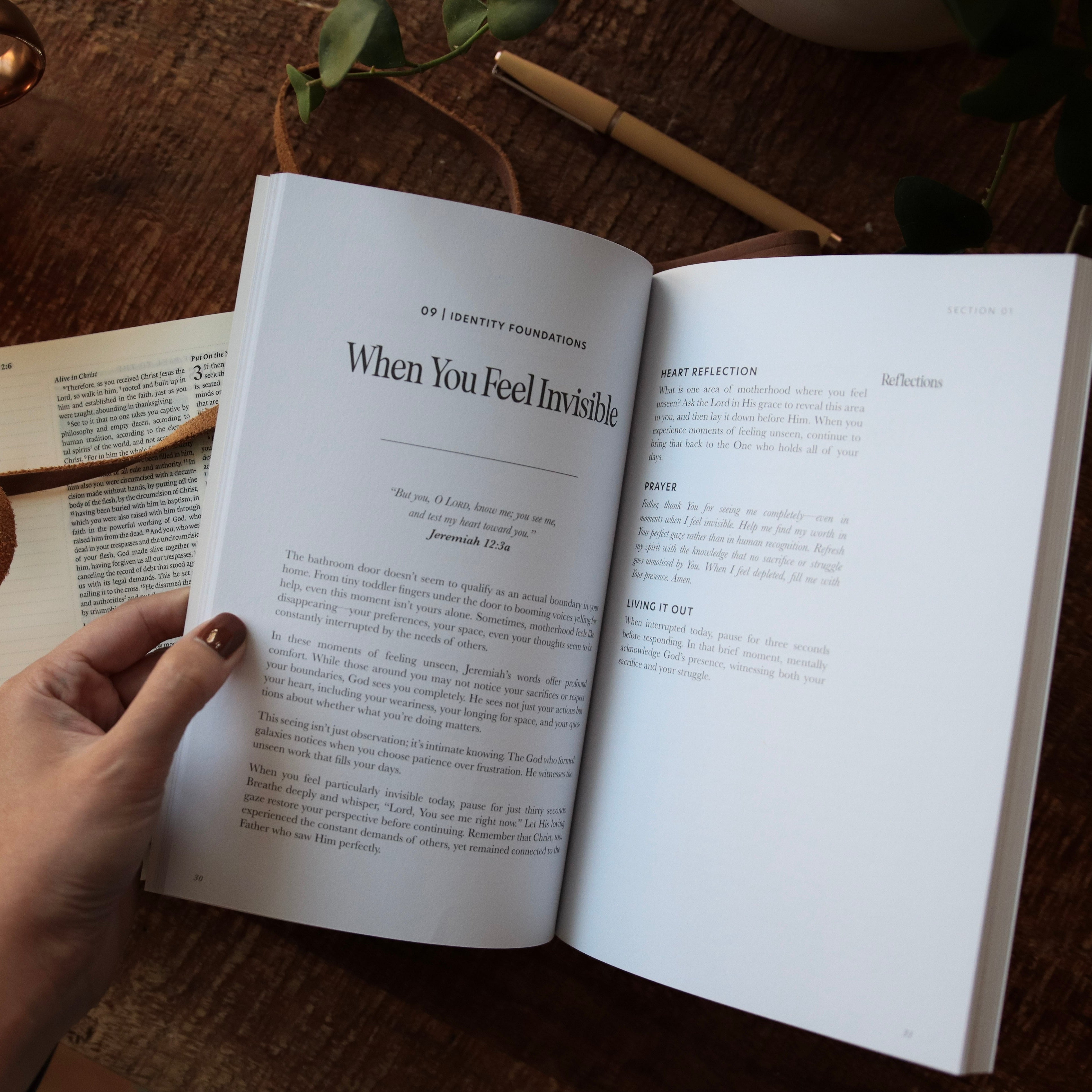 Open book on a wooden table with a hand holding it, next to a cup of coffee.
